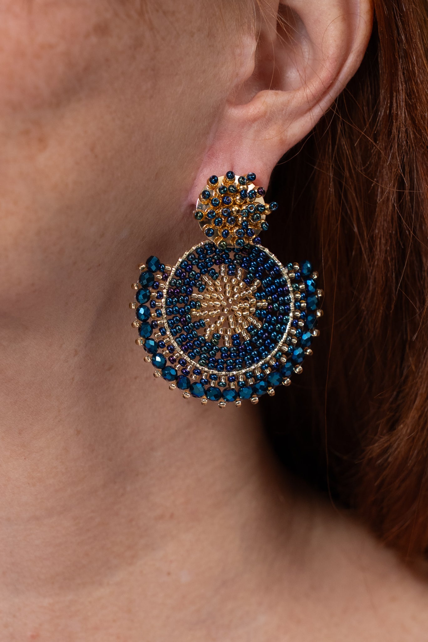 Aros circulares en tonos azul y dorado con diseño tejido y detalle en la parte superior.