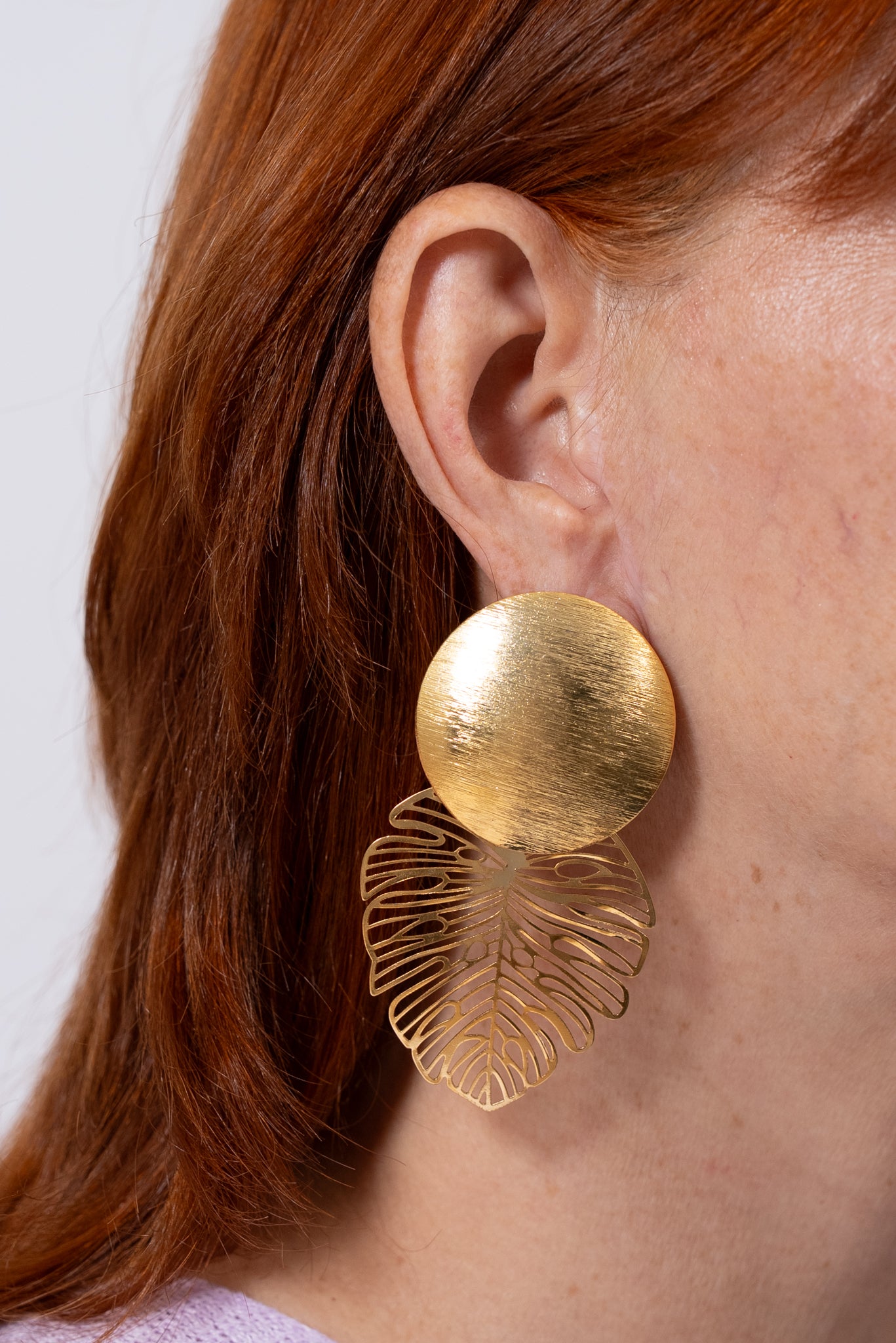 Aros dorados con base redonda grande y colgante tipo hoja calada.