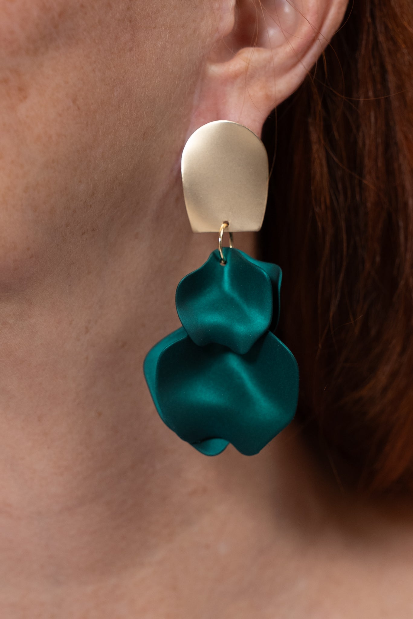 Aros con base dorada mate y colgante verde en forma de pétalos.