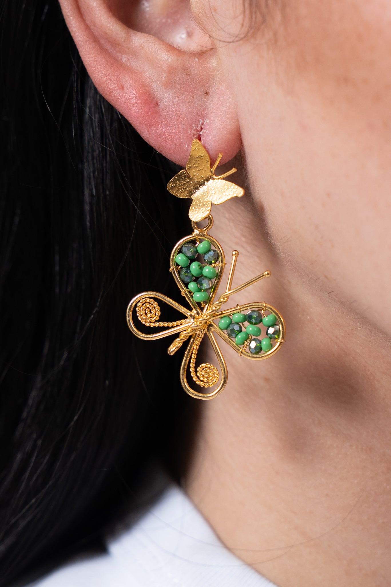 Aros dorados con mariposa grande decorada con cuentas verdes y mariposa pequeña en la parte superior.