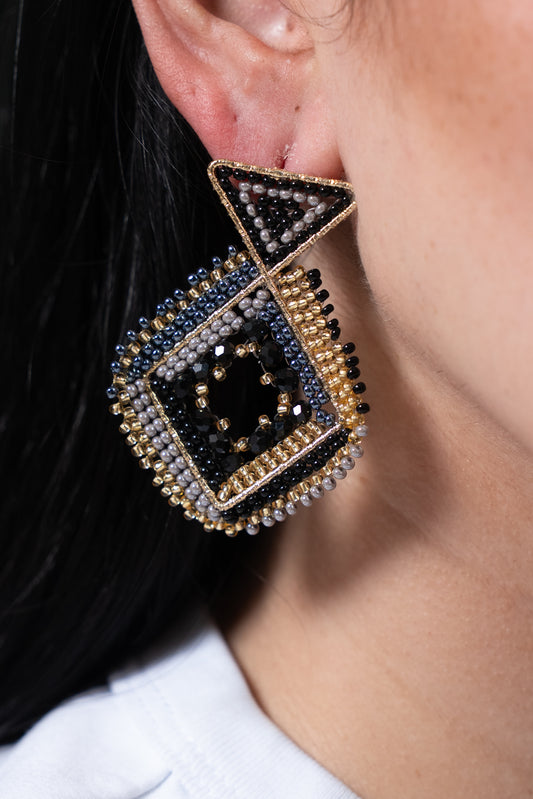 Aros geométricos en tonos negro y dorado con base triangular y colgante cuadrado decorado con cuentas.