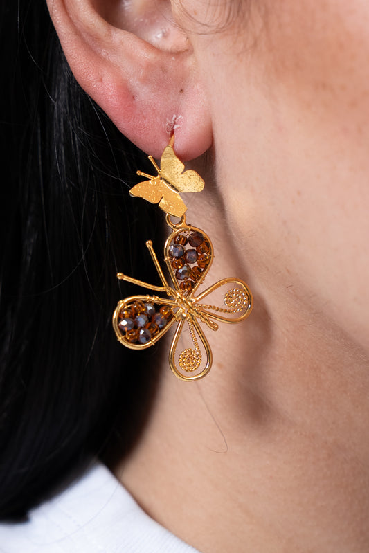 Aros dorados con mariposa grande decorada con cuentas marrones y mariposa pequeña arriba.
