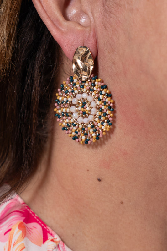 Aros dorados con base metálica y colgante circular tejido en tonos azul, blanco y dorado.