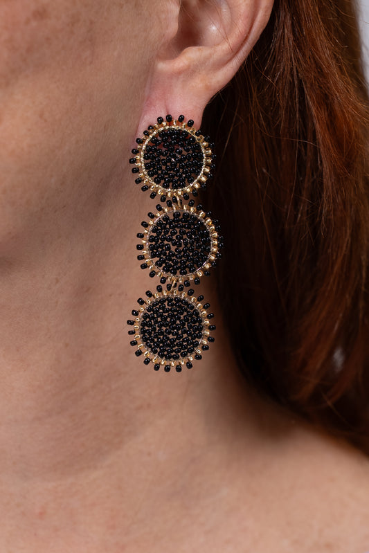 Aros largos dorados con tres círculos tejidos en negro.