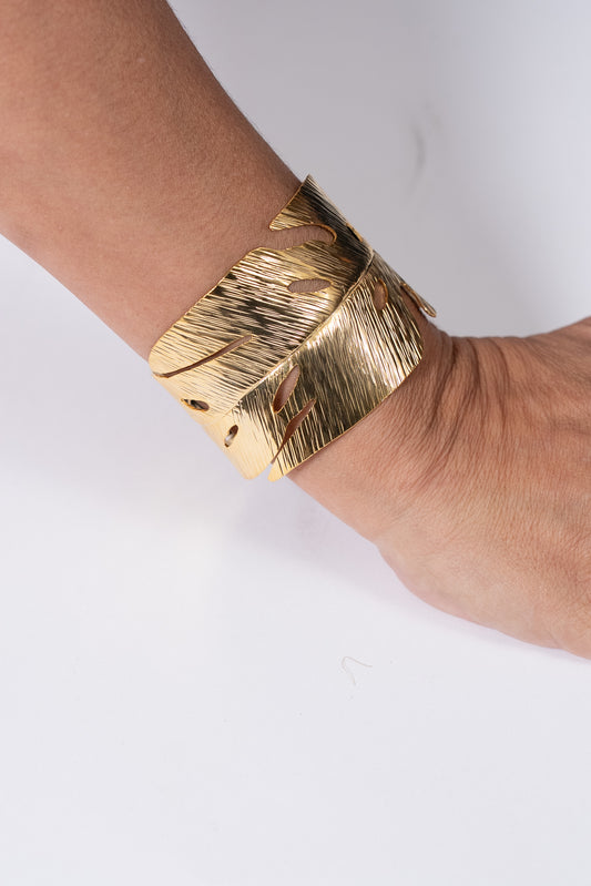 Pulsera dorada ancha con diseño texturado y forma curva.