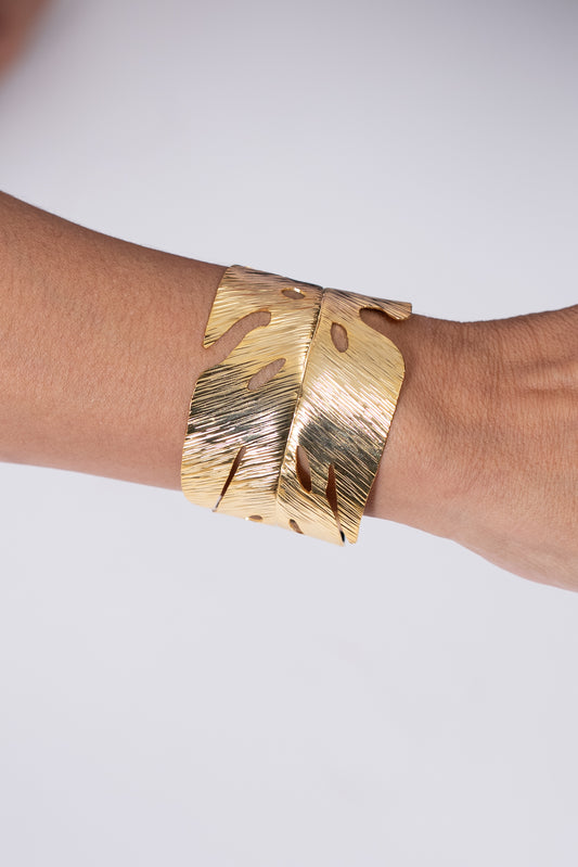 Pulsera dorada ancha con acabado texturado y diseño irregular.