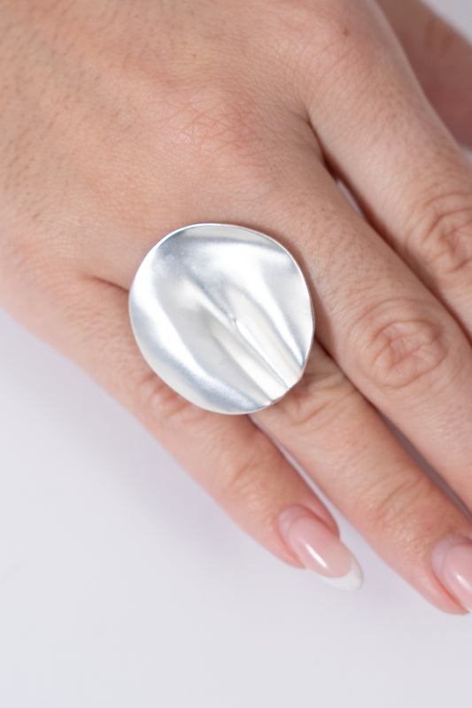 Anillo plateado con pieza circular grande de acabado ondulado.