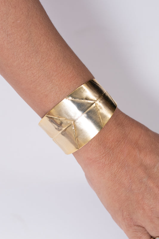 Pulsera dorada ancha con diseño geométrico grabado.