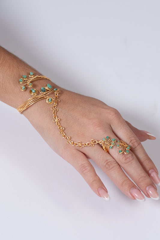 Pulsera dorada tipo esclava con cadena al dedo y detalles verdes.