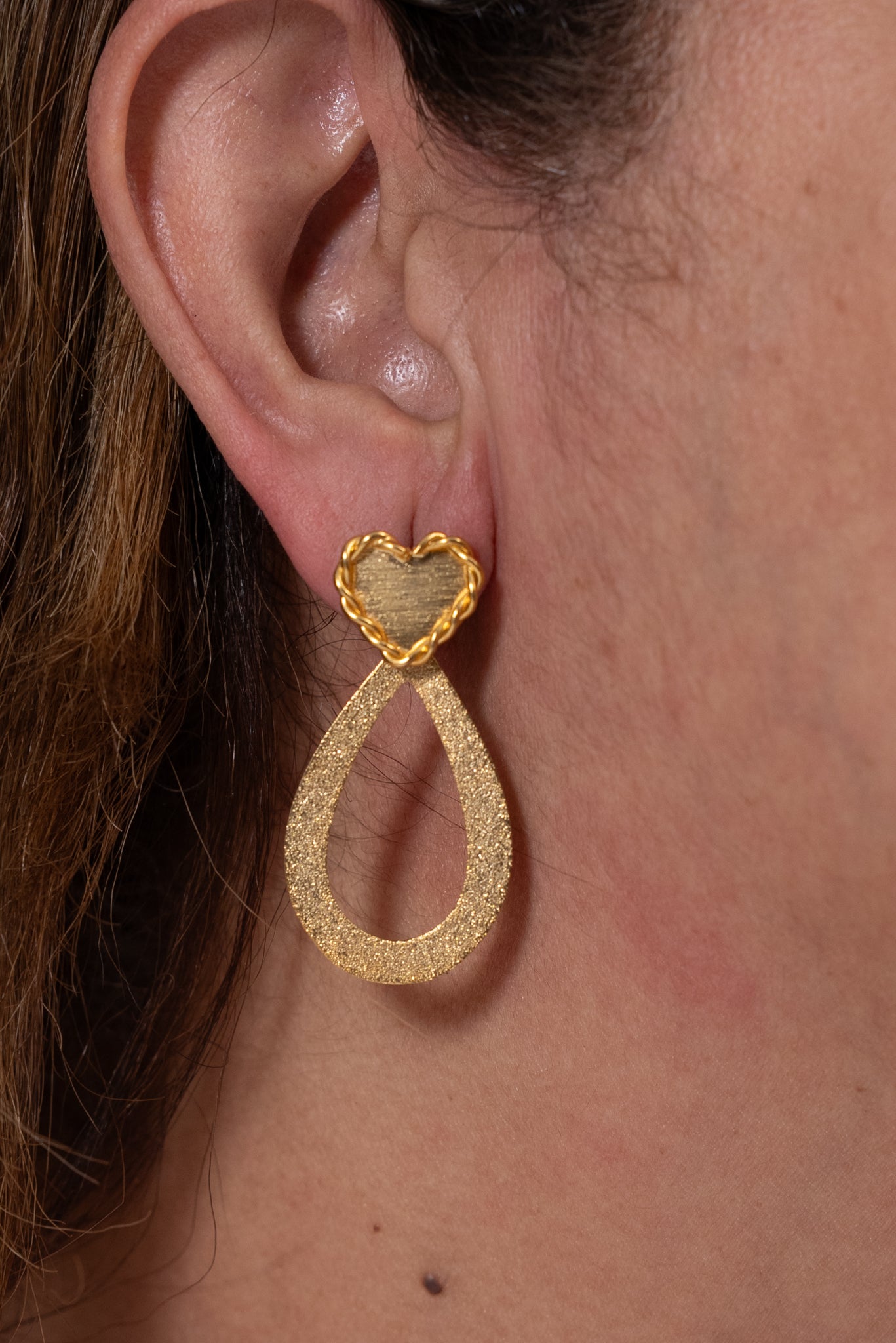 Aros dorados con base de corazón y colgante en forma de gota texturada.