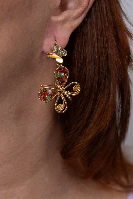 Aros dorados con mariposa grande decorada con cuentas multicolor y mariposa pequeña arriba.