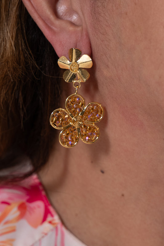 Aros dorados con flor pequeña arriba y flor colgante decorada con cuentas doradas.