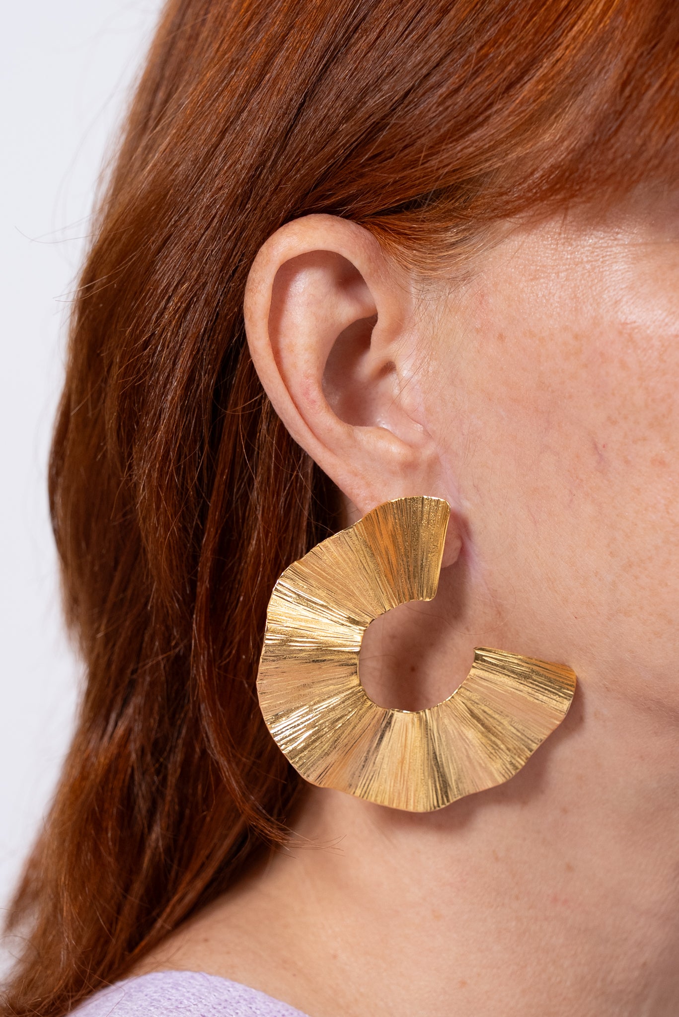 Aros dorados grandes con acabado texturado y forma curva tipo “C”.