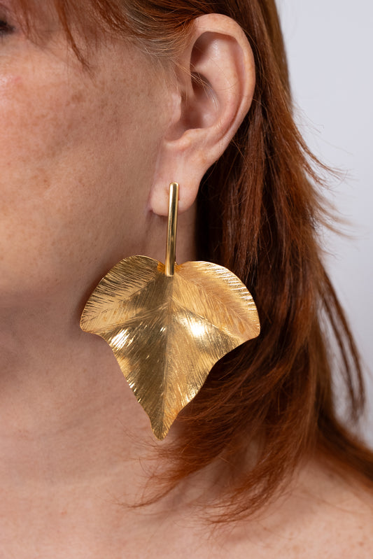 Aros dorados grandes con pieza colgante en forma de hoja.
