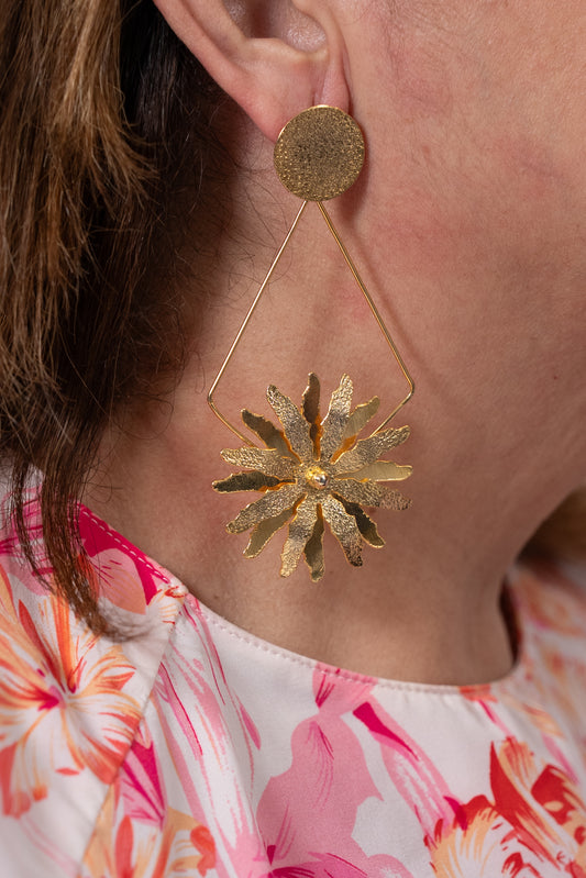 Aros dorados con base redonda y colgante en forma de flor grande unida por estructura triangular.