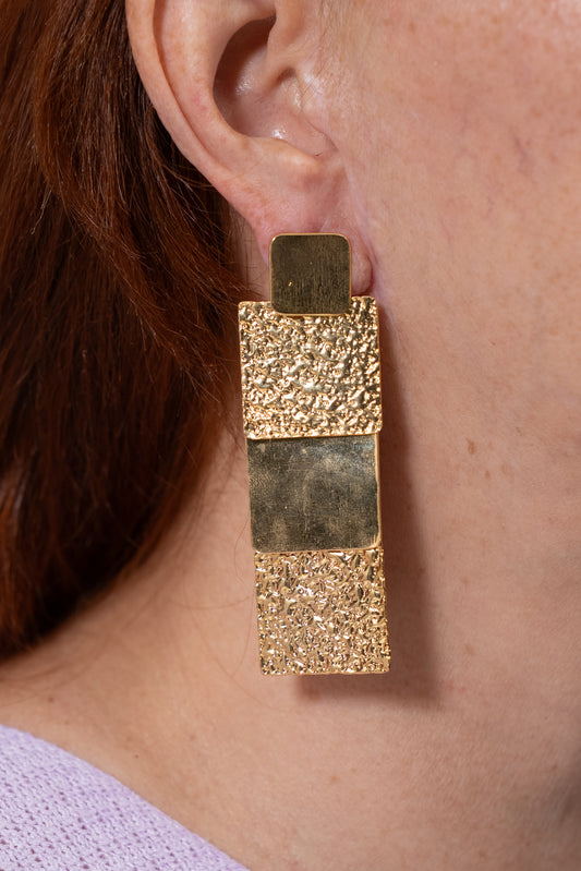 Aretes dorados rectangulares con combinación de textura rugosa y acabado liso.