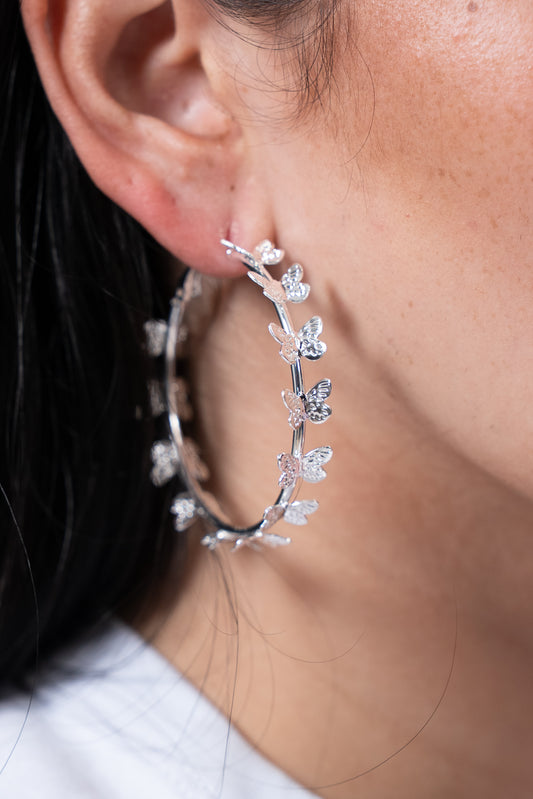 Aros plateados tipo argolla con detalles de hojitas alrededor.