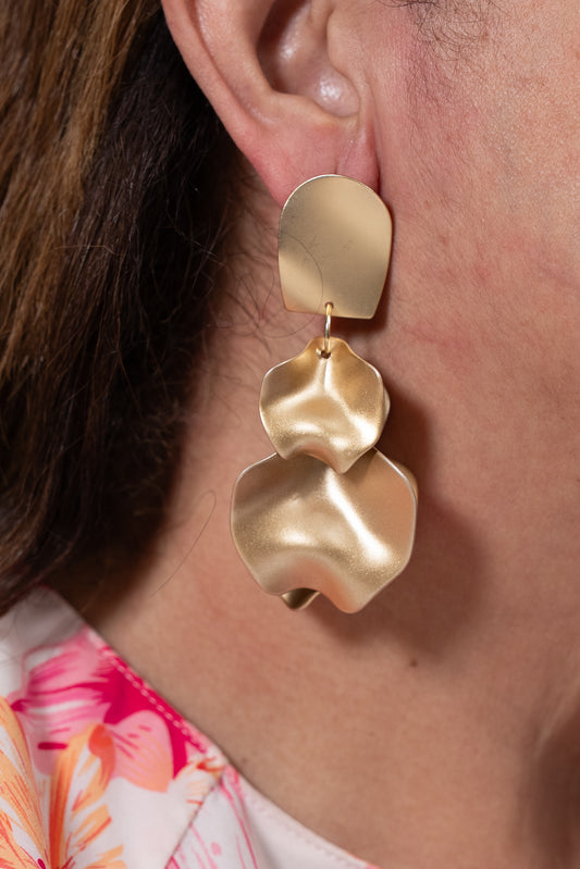 Aros dorados con base mate y colgante metálico ondulado en dos piezas.